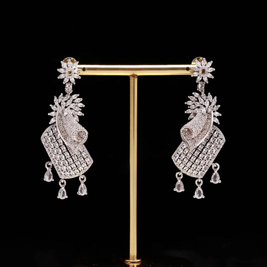 Elegant Haamsi silver earrings with intricate stone detailing and dangling teardrop crystals on display stand